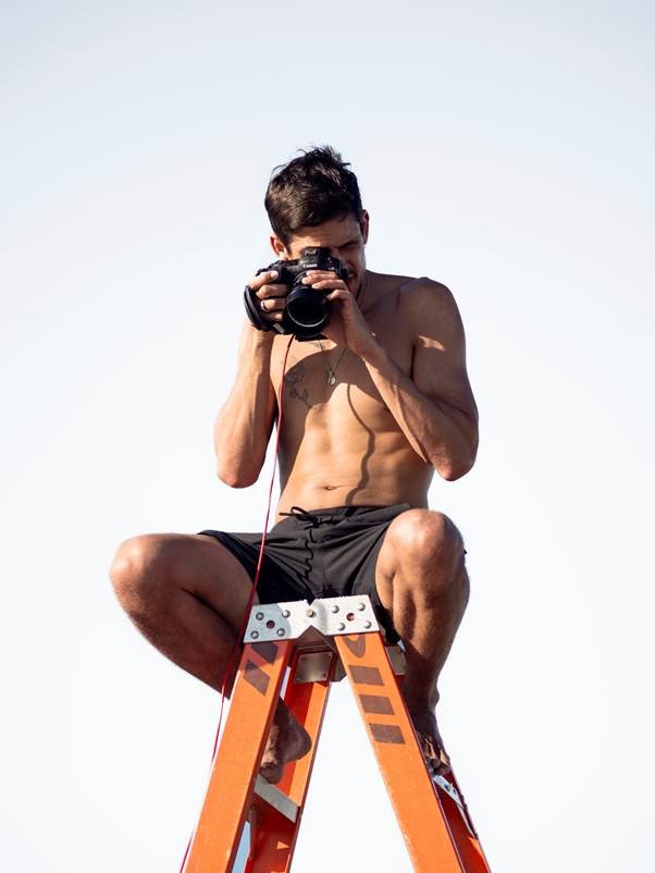 A person sitting on a ladder holding a camera Description automatically generated